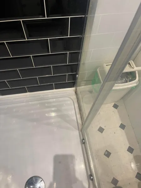 White shower tray and glass screen beside black wall tiles